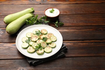 Delicious fried courgette slices with parsley served on wooden table, closeup. Space for text