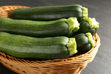 Fresh ripe zucchinis in wicker basket on black table, closeup
