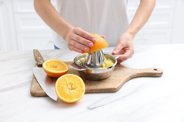 Making juice. Woman with orange using juicer at white marble table indoors, closeup
