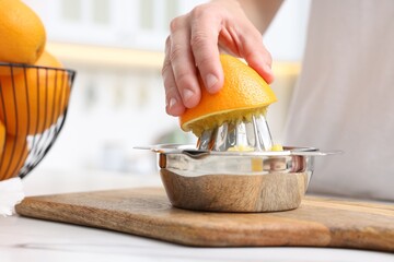 Making juice. Woman with orange using juicer at white marble table indoors, closeup