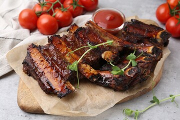 Roasted beef ribs with microgreens, tomatoes and sauce on gray textured table, closeup