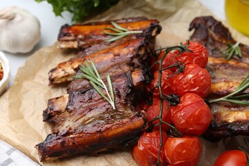 Roasted beef ribs with rosemary and tomatoes on table, closeup