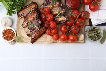 Roasted beef ribs with rosemary, tomatoes and other products on white tiled table, flat lay. Space for text