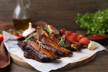 Roasted beef ribs with spices and tomatoes on wooden table, closeup