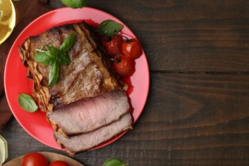 Delicious baked beef meat, tomatoes and basil on wooden table, flat lay. Space for text
