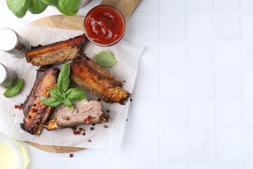 Roasted beef ribs with spices and ketchup on white tiled table, top view. Space for text