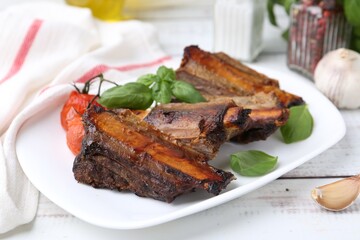 Roasted beef ribs, tomatoes and spices on white wooden table, closeup