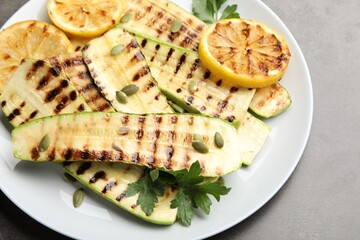 Delicious grilled courgette slices with pumpkin seeds, lemon and parsley on grey table, above view
