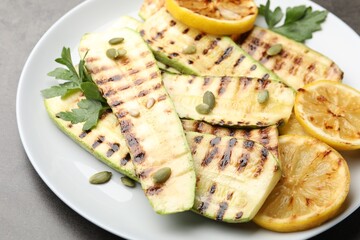 Delicious grilled courgette slices with pumpkin seeds, lemon and parsley on grey table, closeup