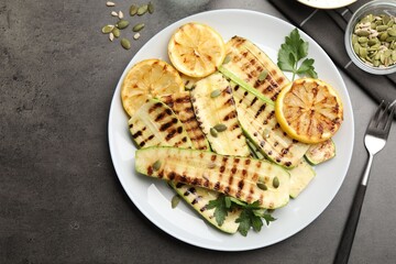 Delicious grilled courgette slices with pumpkin seeds, lemon and parsley served on grey textured table, flat lay