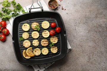 Delicious grilled courgette slices with tomatoes, lemon and parsley in pan on grey textured table, flat lay. Space for text