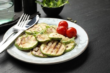 Delicious grilled courgette slices with tomatoes and microgreens served on black textured table, closeup