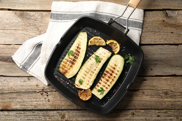 Delicious grilled courgette slices with spices and lemon in pan on wooden table, top view