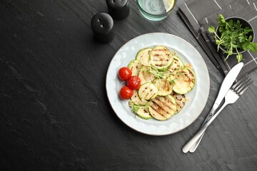 Delicious grilled courgette slices with tomatoes and microgreens served on black textured table, flat lay. Space for text