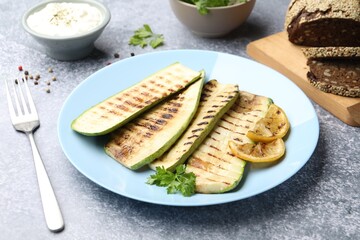 Delicious grilled courgette slices with parsley and lemon served on gray textured table, closeup