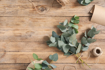 Florist. Eucalyptus branches, thread and wrapping paper on wooden table, flat lay. Space for text
