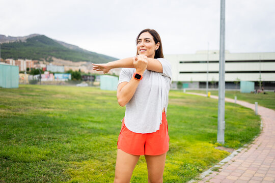 A woman between 40 and 50 years old is exercising outdoors.The woman stretches an arm to the side.Concept of adult women doing sports.