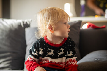 Cute blond boy with long hair in Christmas sweater looking angelic during holiday evening