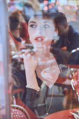 Woman in a black hat and pearls, sitting thoughtfully at a cafe table, with a warm and modern...