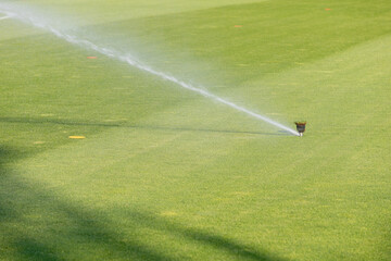 Automatic Sprinkler Watering Lush Green Grass on a Sports Field, Irrigation System for Football...