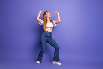 Lovely young woman poses happily on purple backdrop, expressing positive and confident mood in casual and trendy outfit