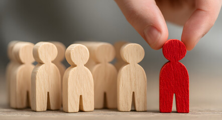 Human resources recruitment concept, hand picking re figure from group of woodn figures
