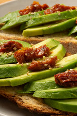 Avocado slices  laying on toasted bread with dried tomato on a white dish. Macro detail.