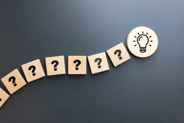 A series of wooden blocks with question marks leading to a light bulb icon, representing the journey from curiosity and uncertainty to a creative idea or innovation
