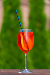 Aperol spritz cocktail in wine glass on a nature background. Classic italian aperitif aperol spritz cocktail with slice of orange. Closeup. Summer refreshing drink with sunlight