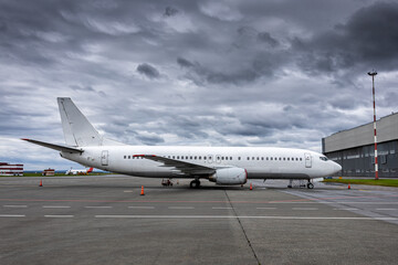 White passenger airliner at airport near airplane hangar in cloudy weather