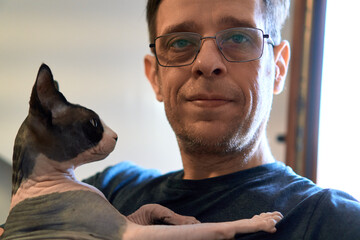 Man with Sphynx cat looking directly at camera indoors