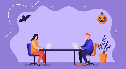 Two colleagues work on laptops at a table, surrounded by a festive Halloween theme with a bat and jack-o'-lantern. Ideal for concepts of holiday work, seasonal business, or tech-savvy Halloween.