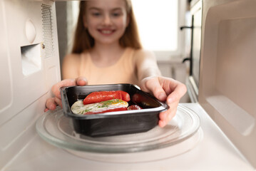 Smiling girl putting ready meal tray into microwave oven, view from inside the appliance.