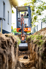 Mini excavator digging a trench next to a house