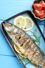 Tasty roasted seabass fish with spices and tomatoes on light blue wooden table, flat lay. Homemade seafood dish
