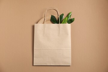 Eco friendly packaging. One paper bag and leaves on light brown background, top view