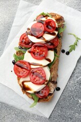 Delicious sandwich with mozzarella cheese, balsamic sauce, tomato and arugula on grey table, top view
