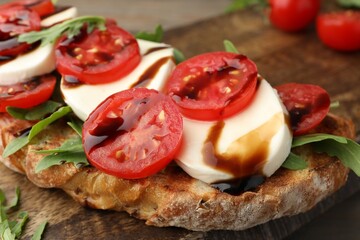 Delicious sandwich with mozzarella cheese, balsamic sauce, tomatoes and arugula on table, closeup