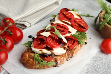 Delicious sandwich with mozzarella cheese, balsamic sauce, tomatoes and arugula on grey table, closeup