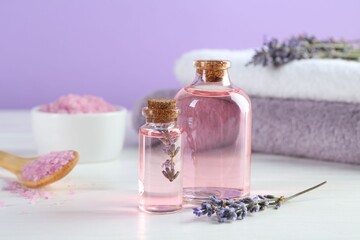 Lavender essential oil, flowers, towels and sea salt on white wooden table, closeup