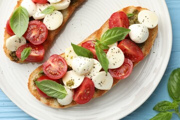 Delicious sandwiches with mozzarella cheese, tomatoes and basil on light blue wooden table, flat lay