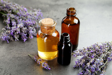 Aromatic essential oil in bottles and lavender flowers on grey textured table, closeup