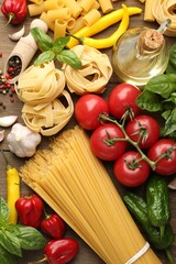 Different types of raw pasta and products on wooden table, flat lay