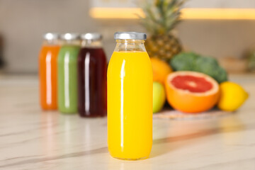 Tasty yellow juice in glass bottle on white marble table indoors, closeup