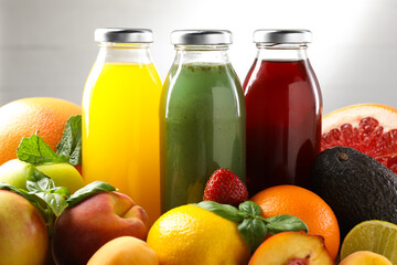 Tasty juices in glass bottles, fresh ingredients and basil against light grey background, closeup