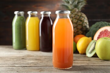 Tasty juices in glass bottles and fresh ingredients on wooden table against brown background, closeup