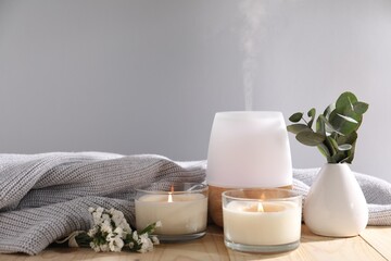 Spa composition with burning candles and aroma oil diffuser on wooden table against light grey...