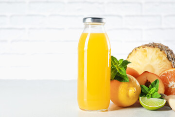 Tasty juice in glass bottle, fresh fruits, ginger and mint on white table against brick wall, closeup. Space for text