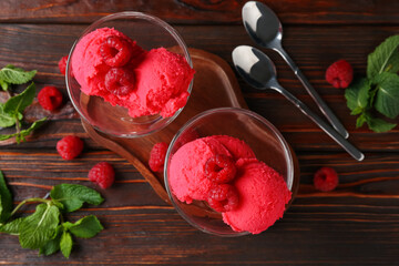 Delicious raspberry sorbet in dessert bowls, spoons, mint and fresh berries on wooden table, flat...