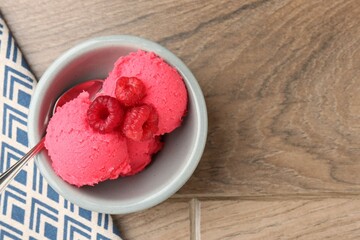 Delicious raspberry sorbet with fresh berries and spoon in bowl on wooden table, top view. Space for text